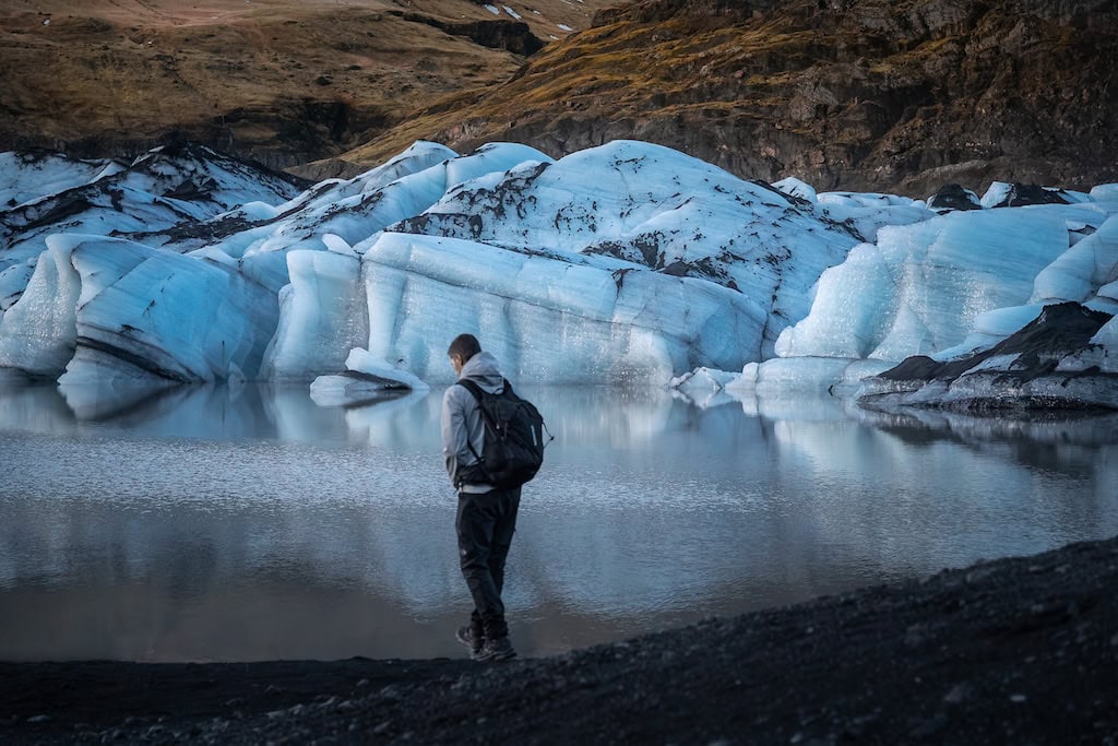 Férfi szürke kabátban sétál a Sólheimajökull gleccserál, Dél-Izlandon