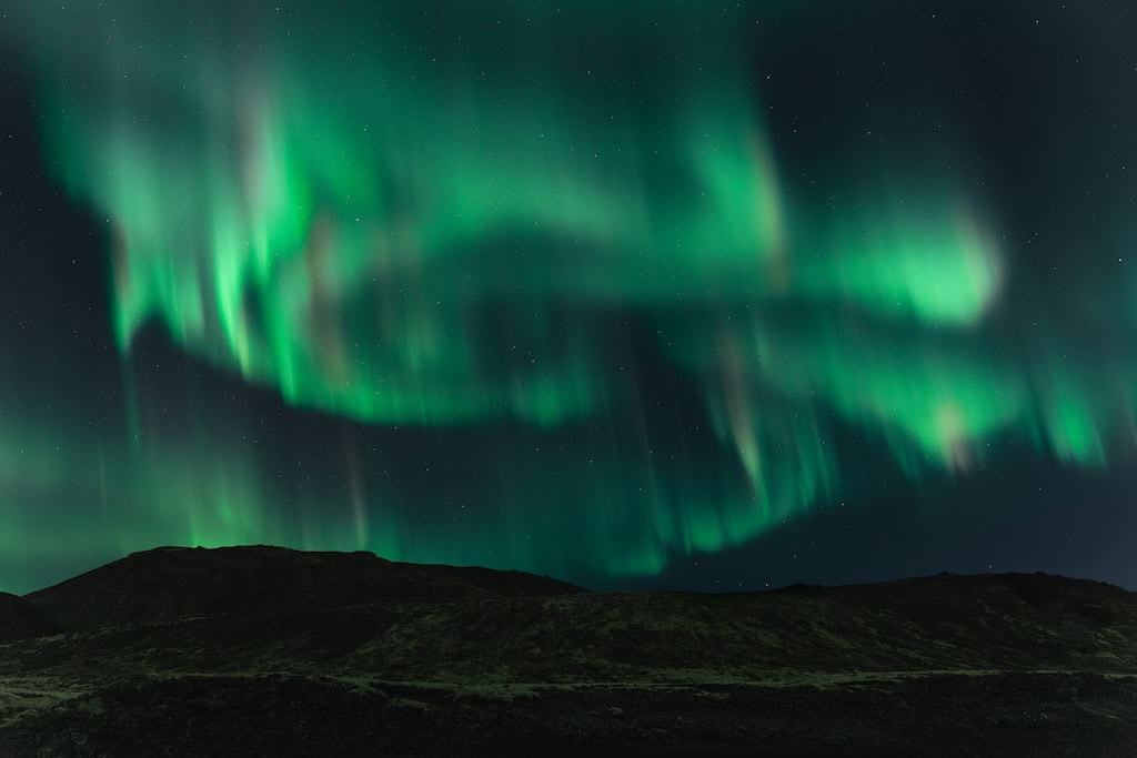 Zölden gomolygó sarki fény a táj felett Izlandon