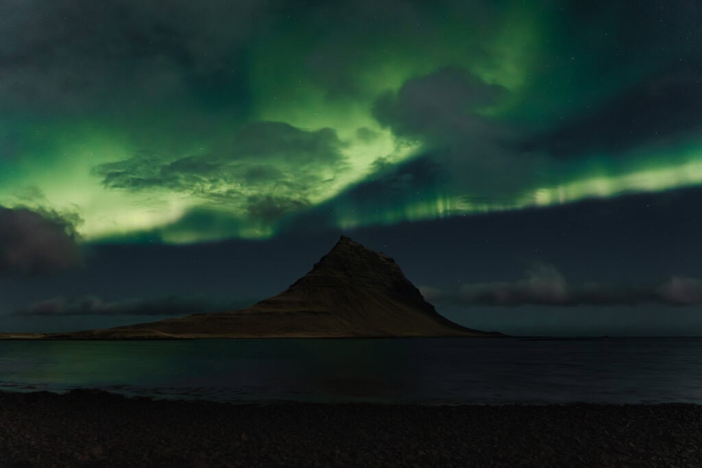 Sarki fény Izland ikonikus Kirkjufell hegyénél, zöld és sárgás fényekkel az égen.