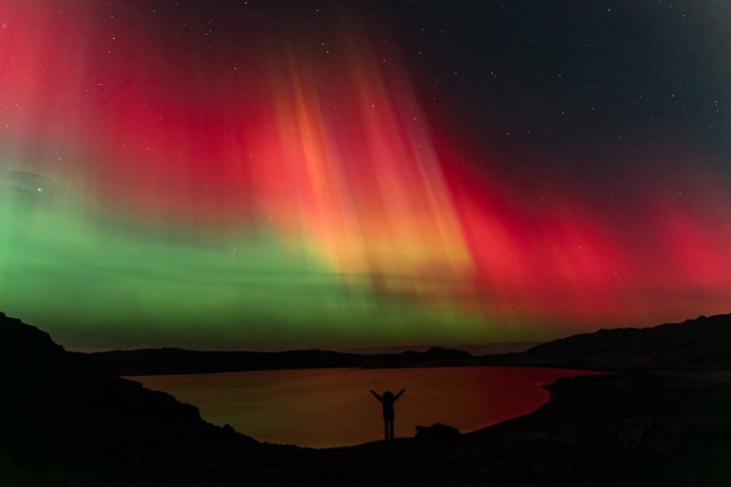Sarki fény Izlandon, markáns vörös és zöld fényívekkel, sötét hegygerinc előtt.