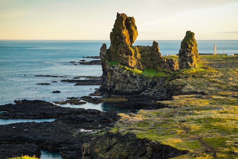 Lélegzetelállító kilátás a Lóndrangar bazaltoszlopokra egy napfényben fürdő, zöld sziklafennsíkról nézve – Snæfellsnes-félsziget nyugati partvidéke, Izland.