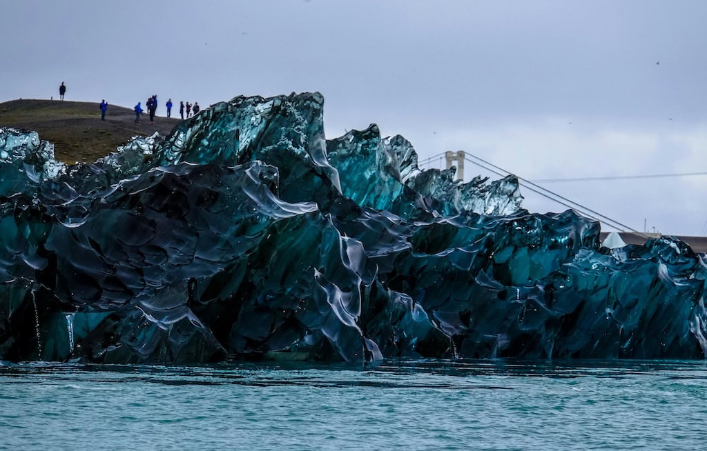 Izland Jökulsárlón gleccserlagúna - kék jégtömbök a vízben a part közelében, háttérben turisták