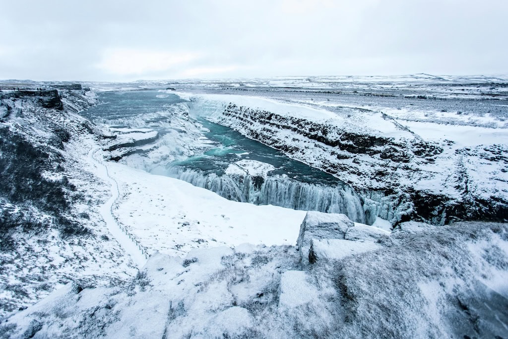 Gullfoss vízesés hóval borított sziklák között – Lenyűgöző kontraszt a mélykék víz és a téli fehér táj között.