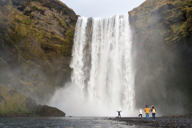 Emberek a hatalmas Skógafoss-vízesés előtt Izlandon, érzékeltetve a vízesés monumentális méretét.