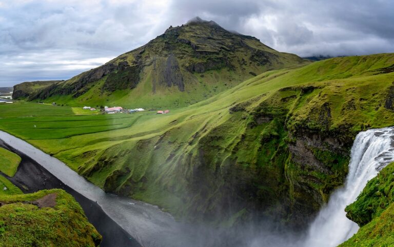 Kilátás a Skógafoss teteján lévő kilátóról, Zöld hegyek és kanyargó út a Skógafoss-vízesés közelében, Izland lenyűgöző déli táján.