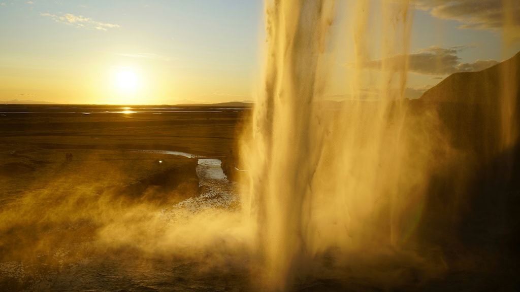Aranyló napfény a Seljalandsfoss-vízesés mögött naplementekor Izlandon.